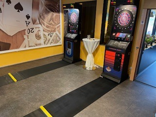 Dart-Automaten in Spielhalle mit Spielkarten-Wandgrafik und gelben Bodenmarkierungen