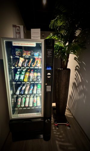 Moderner Verkaufsautomat in elegantem Gaming-Bereich mit Pflanzen und Ambiente-Beleuchtung